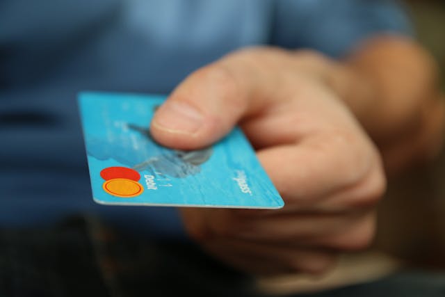 A hand offering a credit card, demonstrating key German shopping vocabulary like 'die Kreditkarte' and 'bezahlen' during a purchase.